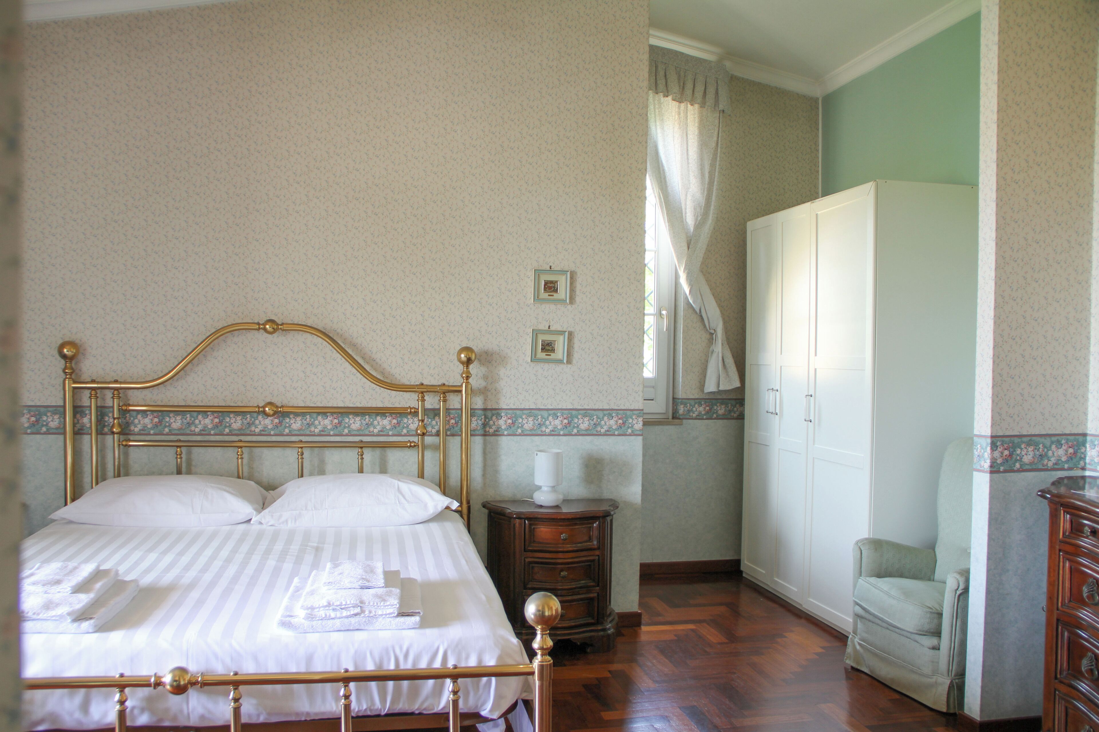 A bedroom with a four-poster bed, a wooden nightstand, a wardrobe, and a chair.