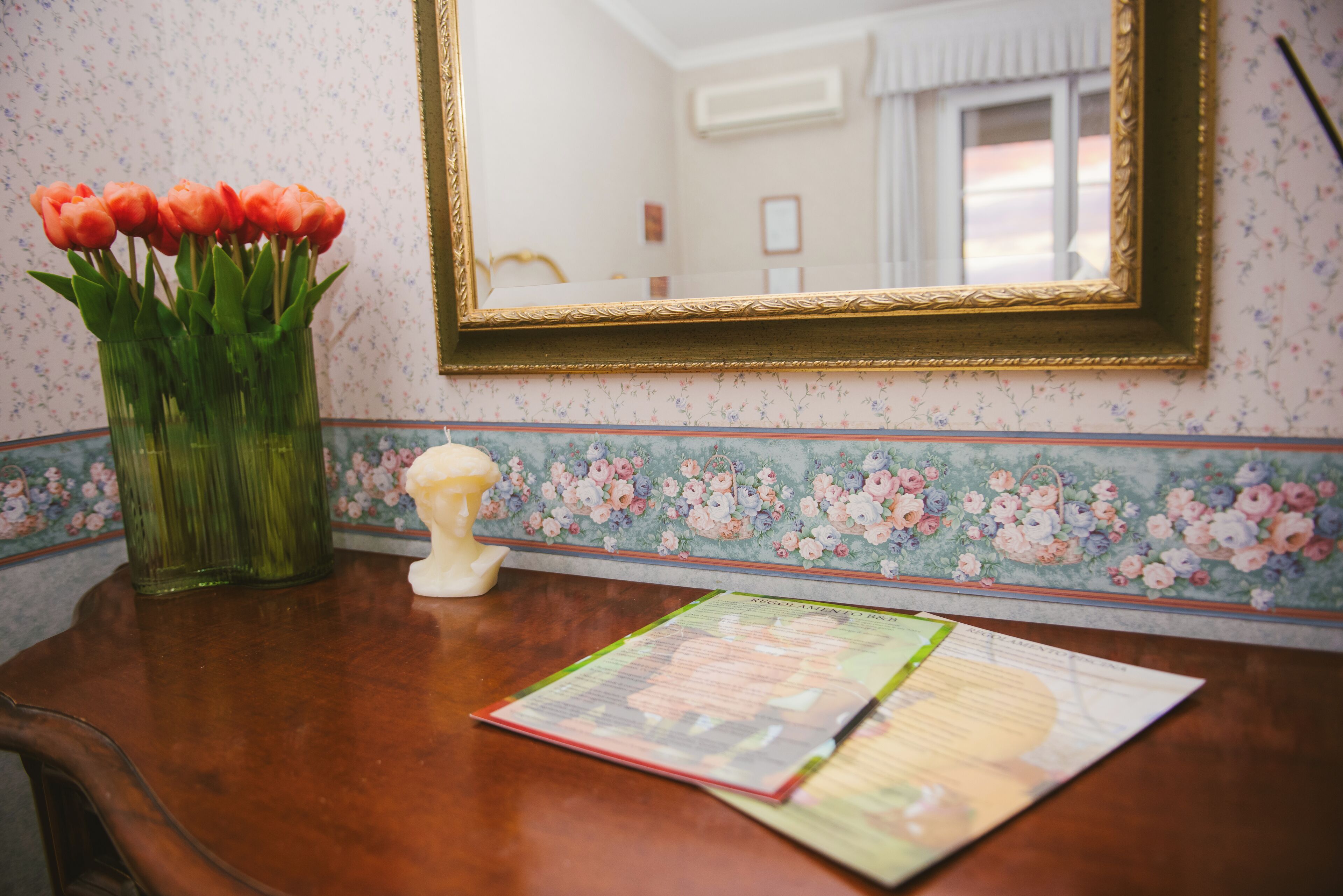 Een houten tafel met een vaas rode tulpen, een buste en een menukaart.