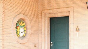 A corner of a building with a green door, a small circular window with a floral design, and a bell mounted on the wall. - Boteroom Relais (Piedimonte San Germano)