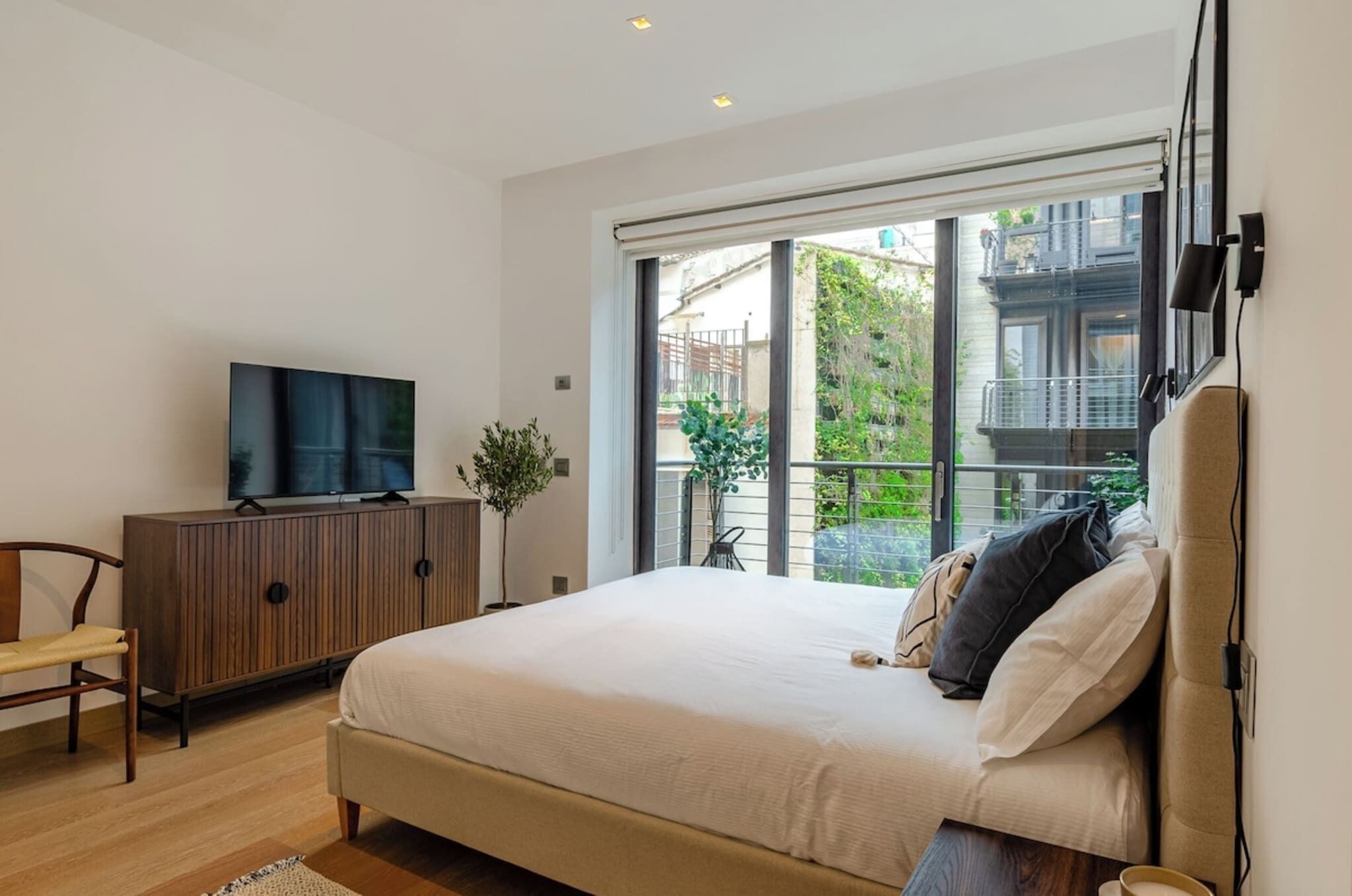 A bedroom with a bed, a TV on a cabinet, a plant, and a balcony with a view.