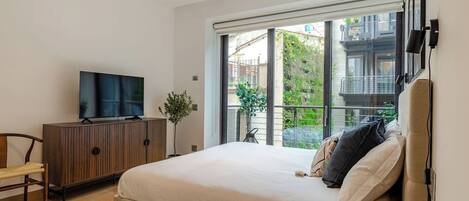 A bedroom with a bed, a TV on a cabinet, a plant, and a balcony with a view.
