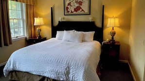 Een net opgemaakt bed met witte lakens, een donker hoofdbord en twee bedlampjes.