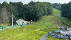 Een berghut met een verhard pad, groen gras en een stoeltjeslift op de achtergrond.