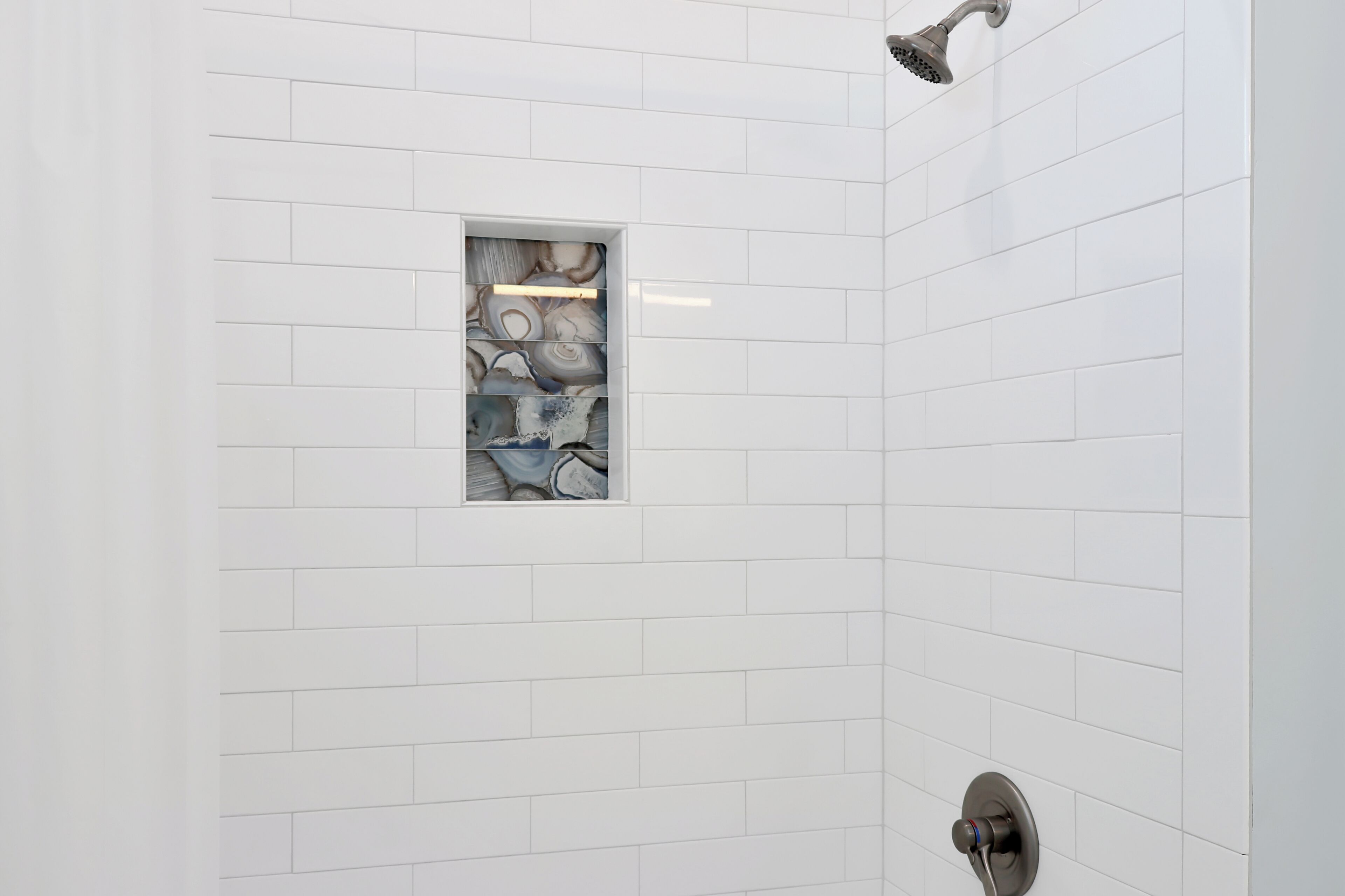 Een douchegedeelte met witte tegels en een inbouwplankje met decoratieve tegels.