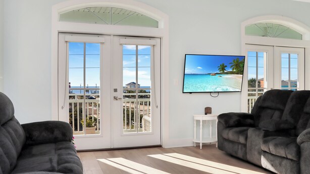 A living room with two dark sofas, a flat-screen TV on the wall, and a balcony door. - 🌊Dog Friendly Home with Private Pool-Steps to the Beach-Salty Owl🌊 (Cape San Blas)