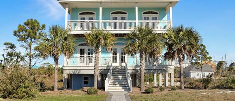 A two-story house with a front porch, a staircase leading to the second floor, and palm trees in the yard.