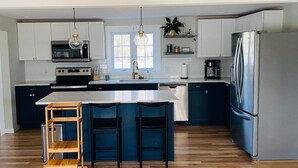 A modern kitchen with a central island, stainless steel appliances, and wooden flooring. - Spacious Charming Kennebunk Home (Kennebunk)