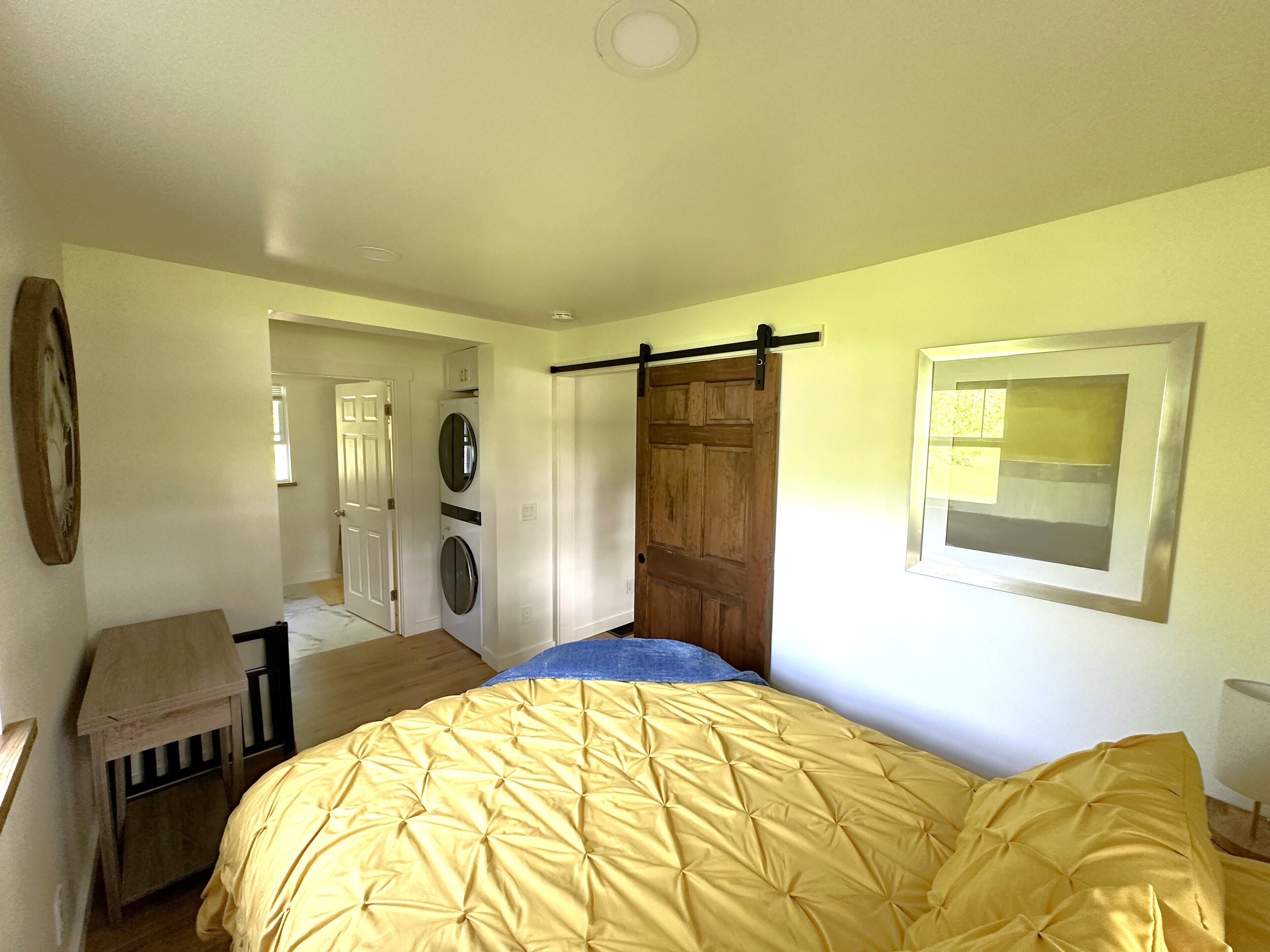 Een slaapkamer met een bed, een houten deur, een wasmachine en een klein tafeltje.