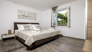 A bedroom with a large bed, a nightstand, a window with a view of greenery, and a painting on the wall. - Apartments Mi&Ni -Comfort Two Bedroom Apartment with Terrace and Sea View (no.3) (Cavtat)