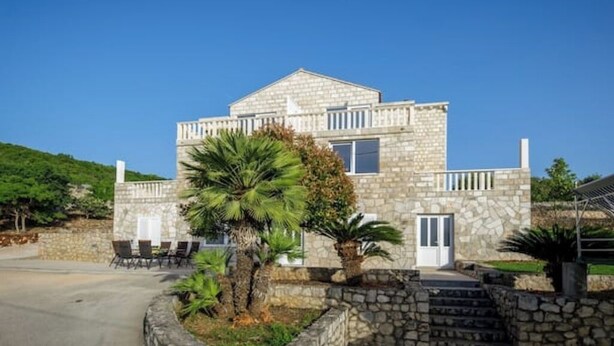 A stone building with a balcony, a door, and a small patio with chairs and a palm tree. - Apartments Mi&Ni -Comfort Two Bedroom Apartment with Terrace and Sea View (no.3) (Cavtat)