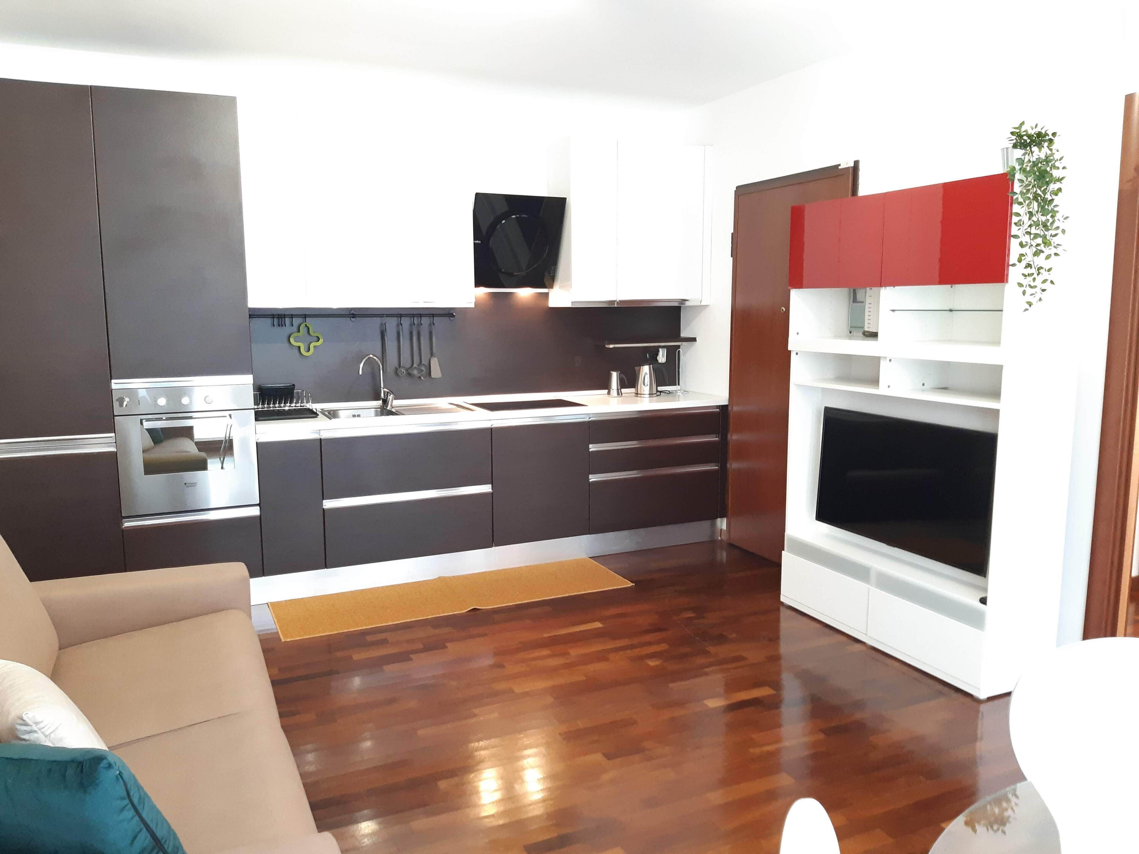 A modern kitchen with dark cabinets, stainless steel appliances, and a red accent wall.