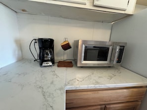 Une cuisine équipée d’une machine à café, d’un four à micro-ondes et d’un bloc de bois posé sur le plan de travail.