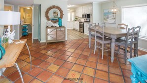 A spacious kitchen with white cabinets, a dining table with chairs, and a tiled floor.