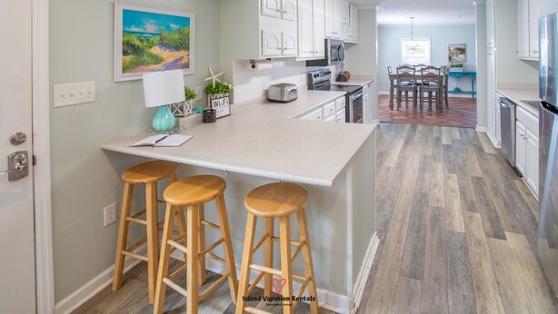 A kitchen with a central island, wooden stools, white cabinets, and a painting on the wall.