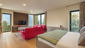A modern bedroom with a bed, a red sofa, a TV, and large windows offering a city view.