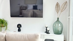 Un salon moderne avec un téléviseur à écran plat fixé au mur, un grand vase orné de feuilles décoratives et une petite sculpture noire posée sur une console blanche.