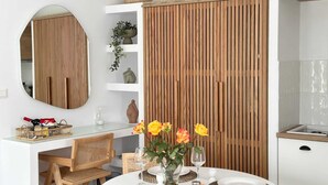 Une cuisine moderne avec des meubles blancs, un séparateur en panneaux de bois, une table de salle à manger ronde agrémentée d’un vase de fleurs et un panier en osier posé sur le comptoir.