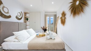 A neatly made bed with white linens, a bedside table with a tray of toiletries, and a large window with curtains. - Villa Grande Casa with Pool, Villa Grande Casa with Swimming Pool (Corfu)