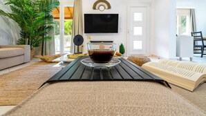 A living room with a sofa, a coffee table with a book and a glass of red drink, a TV, and a large plant. - Villa Grande Casa with Pool, Villa Grande Casa with Swimming Pool (Corfu)