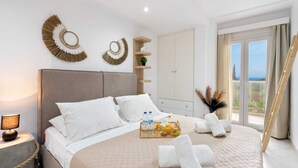 A modern bedroom with a large bed, a bedside table with a lamp, a tray with toiletries, and a view of the sea through the window. - Villa Grande Casa with Pool, Villa Grande Casa with Swimming Pool (Corfu)