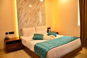 Une chambre d’hôtel moderne avec une tête de lit en marbre, un grand lit avec une literie de couleur turquoise, une table de chevet avec un téléphone et une lampe, et une petite table de nuit avec un tiroir.