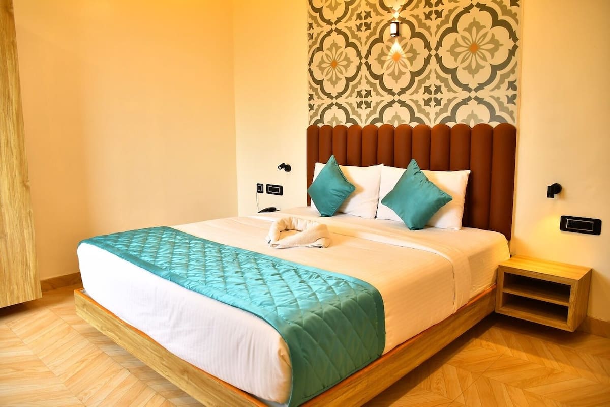 A neatly made bed with a teal quilt, a wooden headboard, and a patterned wall behind it.