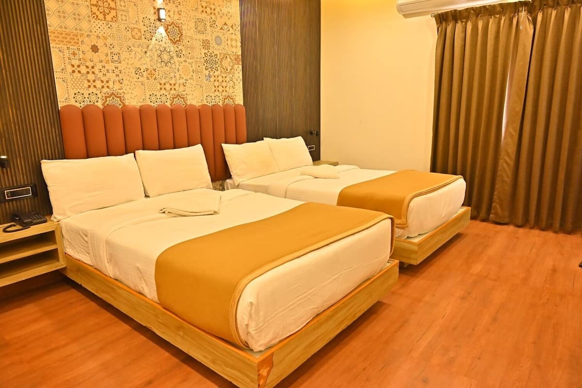A hotel room with two beds, wooden headboards, a patterned wall, and a window with curtains.