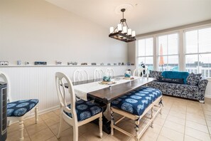 A dining area with a long table, white chairs, and a patterned sofa. - Mini Weeks Stays Available Sunset Island 39 Island (Ocean City)