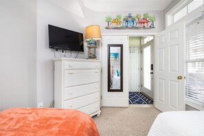 A bedroom with a bed, a dresser, a television, a lamp, and a door leading to another room. - Mini Weeks Stays Available Sunset Island 39 Island (Ocean City)