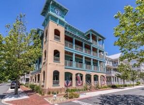 A multi-story building with a clock tower, balconies, and American flags. - Mini Weeks Stays Available Sunset Island 39 Island (Ocean City)