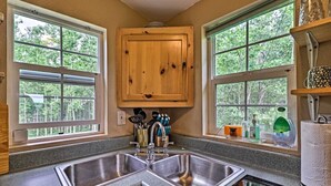 A kitchen with two sinks, wooden cabinets, and windows with a view of trees. - Duck Lake Cabin Rental Near GNP (Babb)