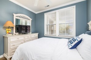 Une chambre à coucher avec un lit, une commode, un miroir, une lampe et une fenêtre avec des stores.