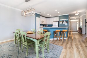 Une cuisine moderne avec des meubles blancs, un îlot central bleu et un coin repas avec des chaises vertes.