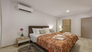 Une chambre moderne avec un grand lit, une table de chevet, un climatiseur et une armoire en bois.