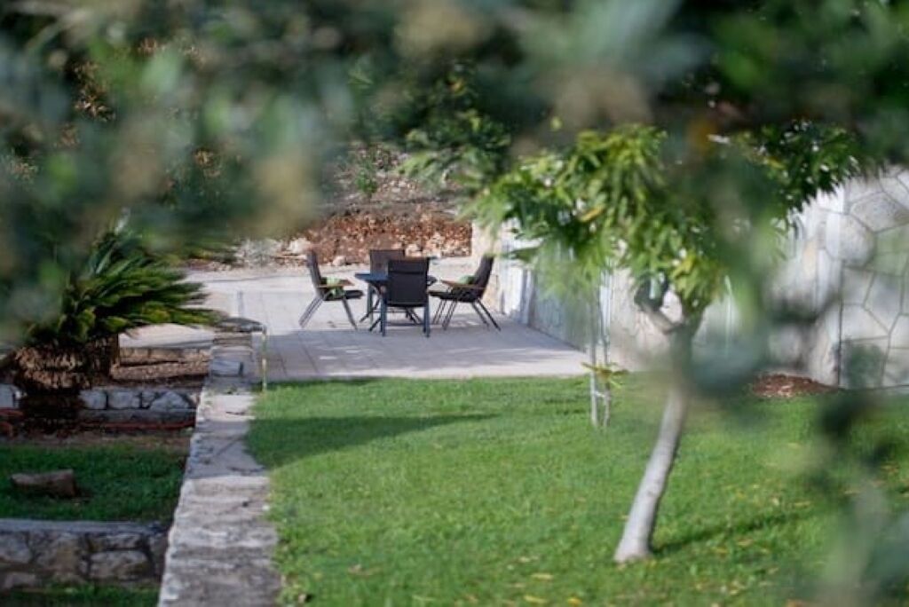 A patio area with a table and chairs, surrounded by a stone wall and greenery.