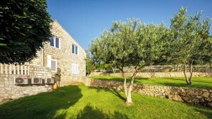 Une maison en pierre avec une pelouse bien entretenue et un arbre au premier plan.