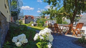 Un jardín con flores blancas, un sendero de grava y una mesa de madera con sillas.