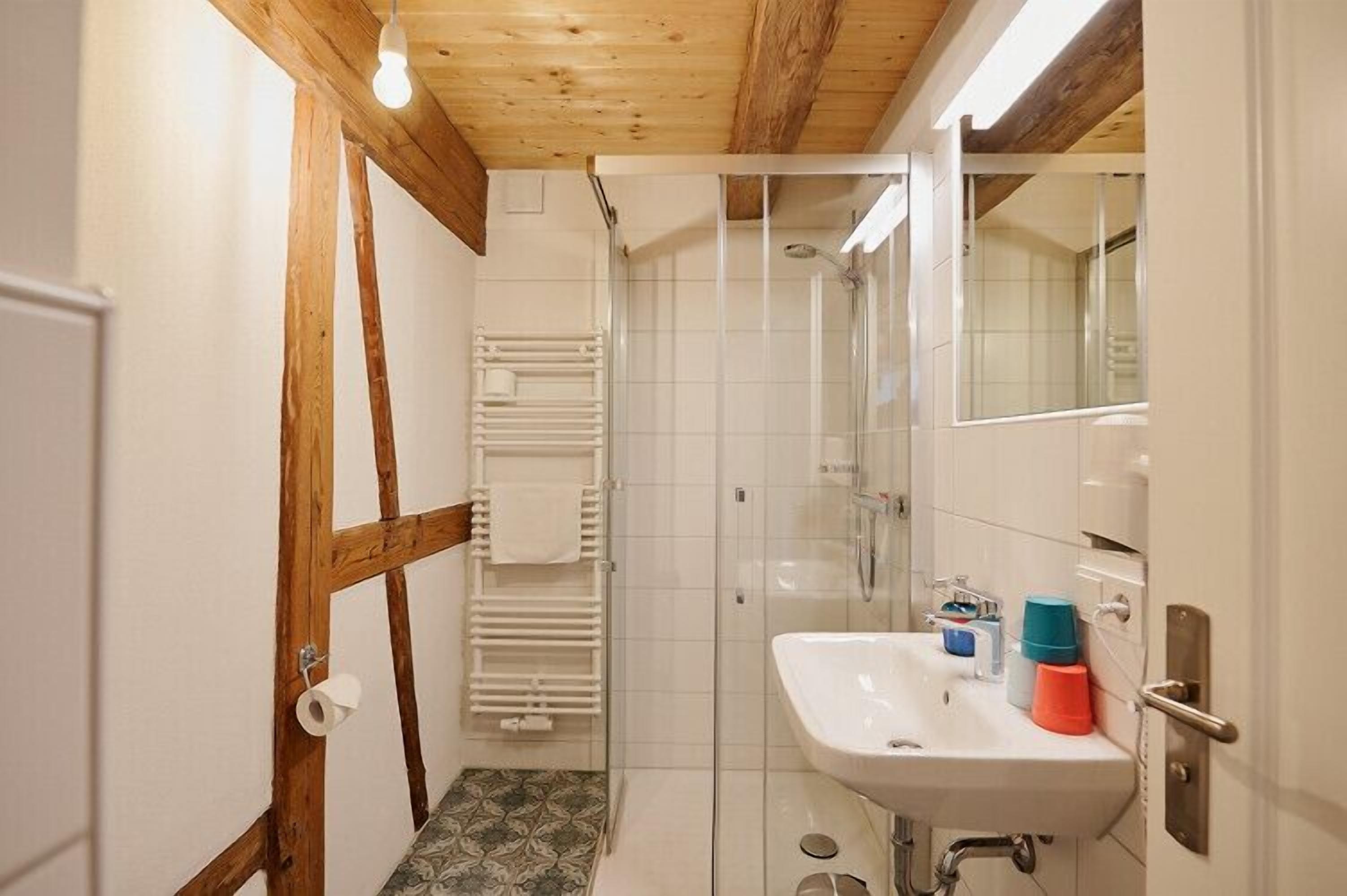 Un baño con techo de madera, cabina de ducha de vidrio, lavamanos blanco y barra para toallas.
