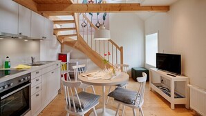 Una cocina moderna con armarios blancos, una escalera de madera y un comedor con sillas y una mesa blancos.