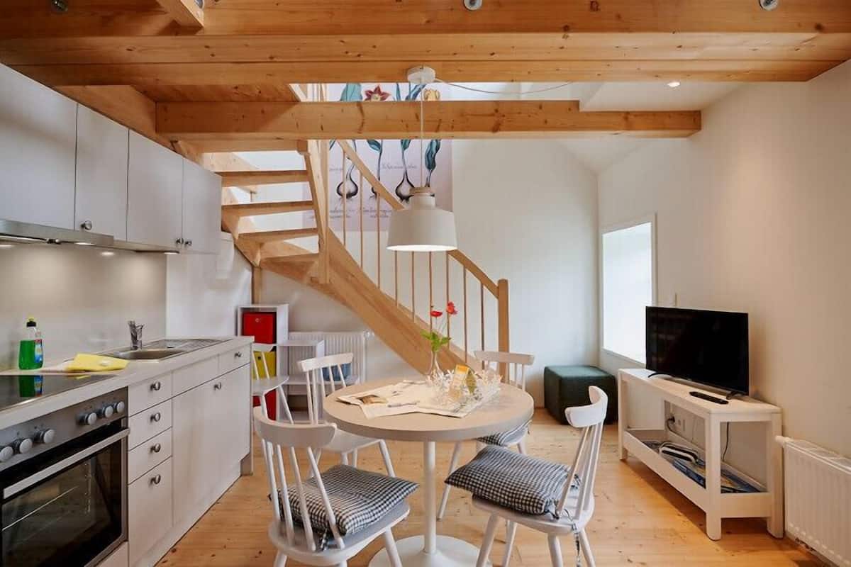 Een moderne keuken met witte kasten, een houten trap en een eethoek met witte stoelen en een tafel.