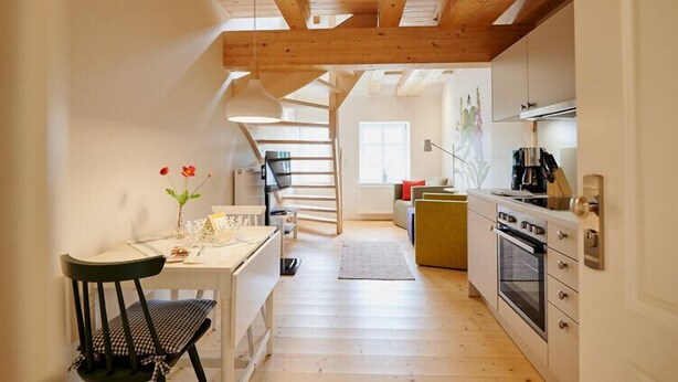 Una cocina moderna con vigas de madera, un comedor con mesa y sillas, y una escalera que conduce a otro nivel.