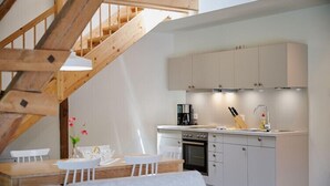 Una cocina moderna con armarios blancos, una escalera de madera y un comedor con mesa y sillas.