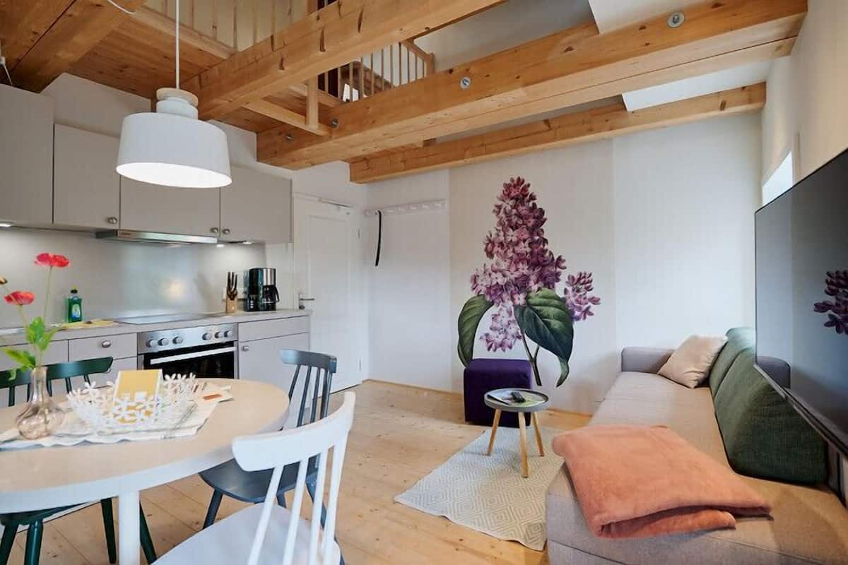 Een moderne keuken met witte kasten, een eettafel met stoelen, een bank en een groot raam.