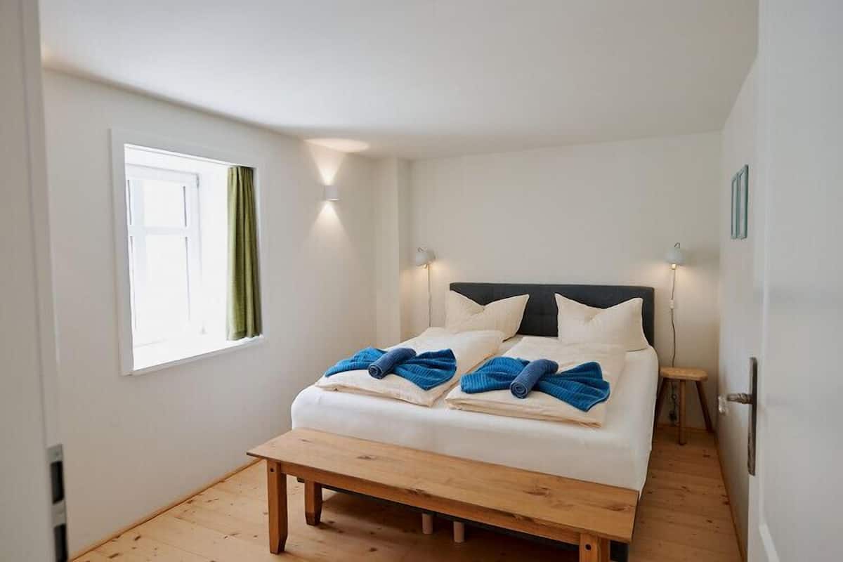 Een slaapkamer met een bed, bedlampjes, een raam en een houten bank.