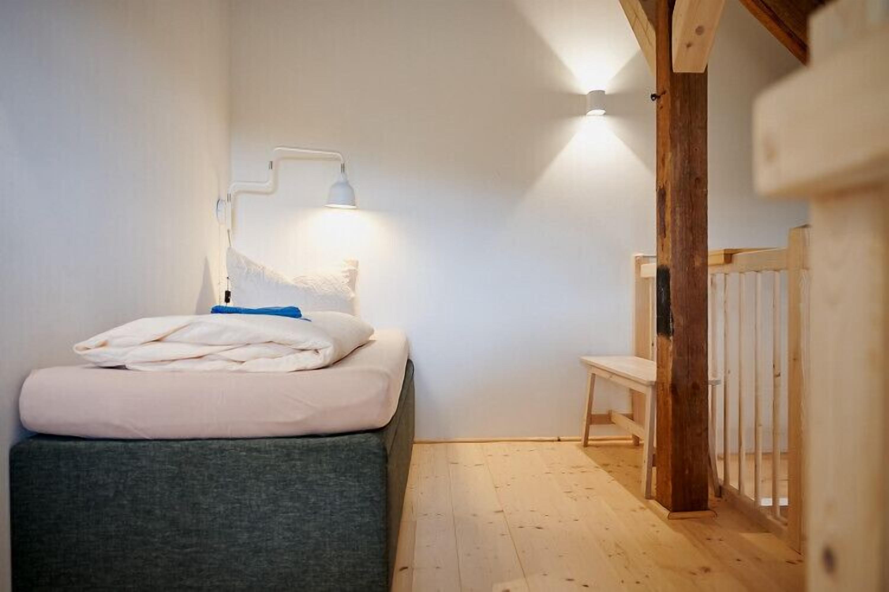 A bedroom with a bed, a bedside table, a lamp, and a wooden bench.