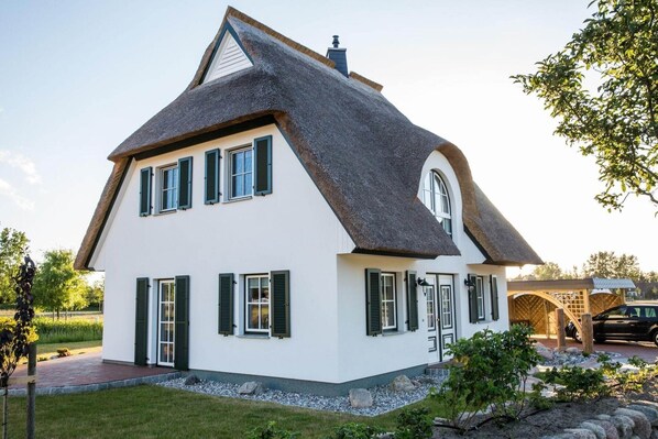 A two-story house with a steeply pitched roof, multiple windows with shutters, and a well-maintained garden.