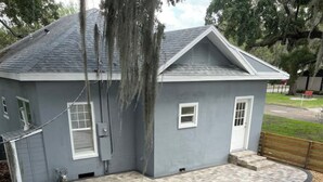 Una casa con fachada gris, un patio cubierto con pavimento estampado y una valla de madera.