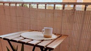 A wooden table with a woven placemat and a white mug, a woven plant pot, and a white knitted bench on a wooden deck. - Gilmore Home - close to Paris center (La Courneuve)