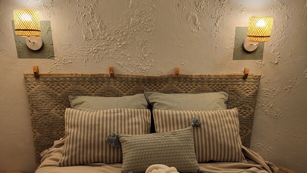 A bed with a woven headboard, multiple pillows, and a textured wall. - Gilmore Home - close to Paris center (La Courneuve)