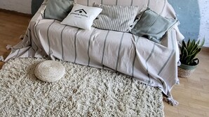 A sofa with striped fabric and multiple pillows, a textured rug, and a small potted plant. - Gilmore Home - close to Paris center (La Courneuve)